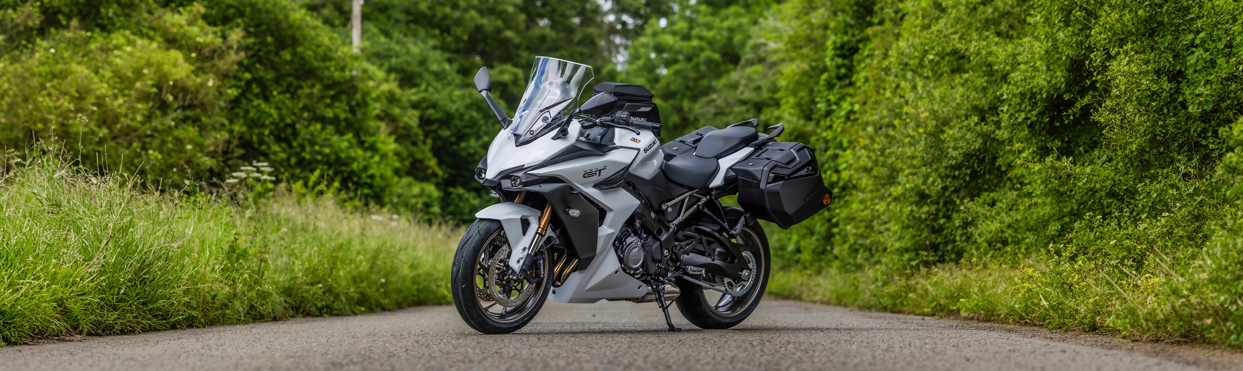 Suzuki GSX-S1000GT+ white static left hand side front three quarters with trees behind