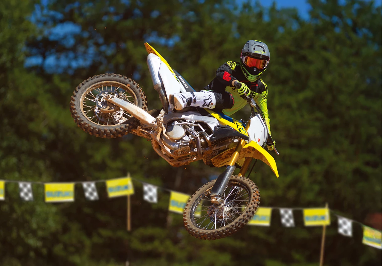 Suzuki RM-Z250 whip over a jump with trees in the background