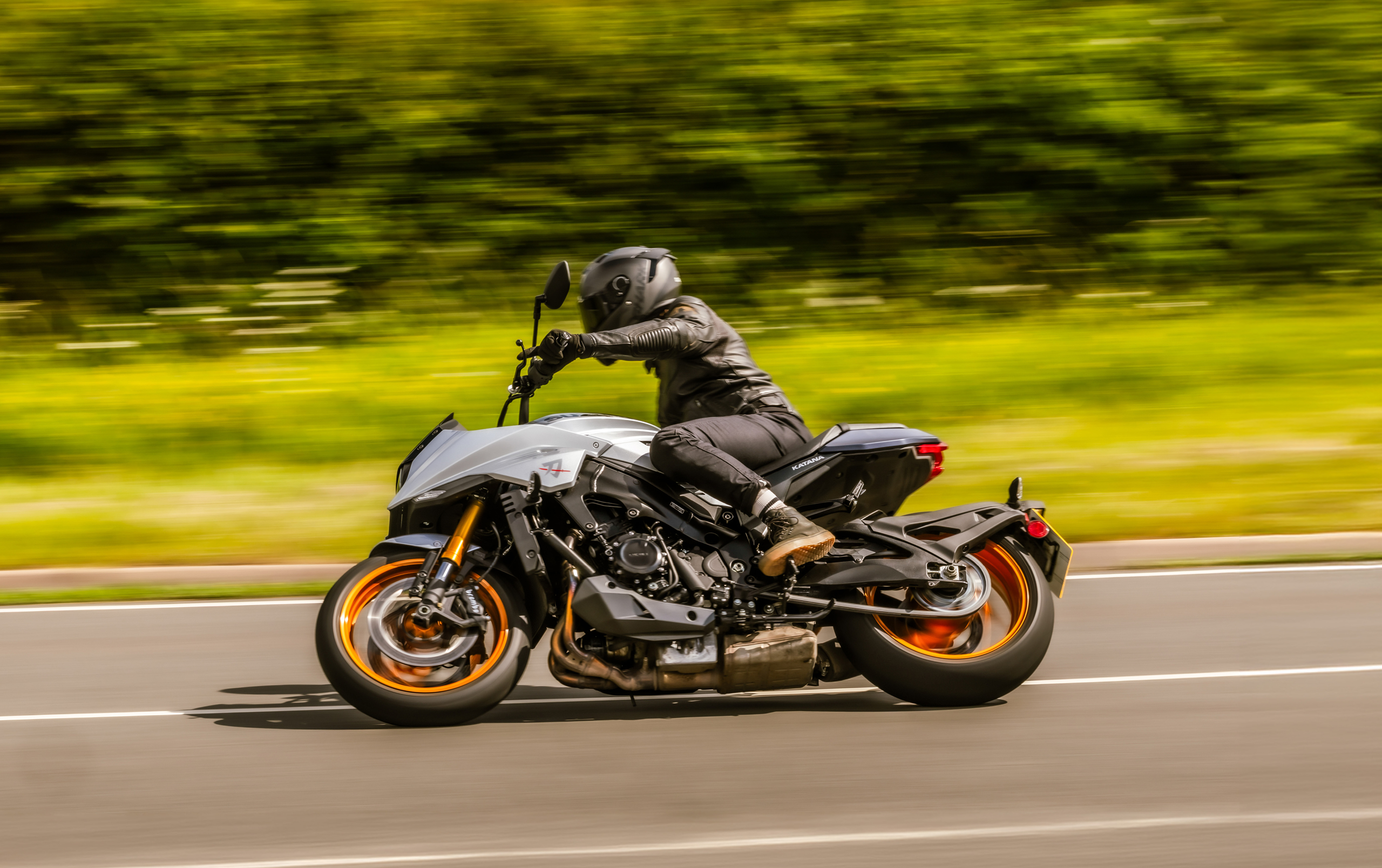 Suzuki Katana silver leaning hard into a corner with grass and bushes behind