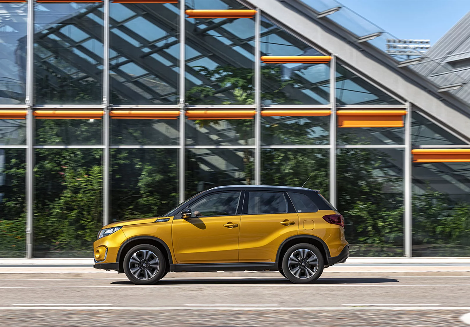 Solar yellow Suzuki Vitara parked in front of a greenhouse