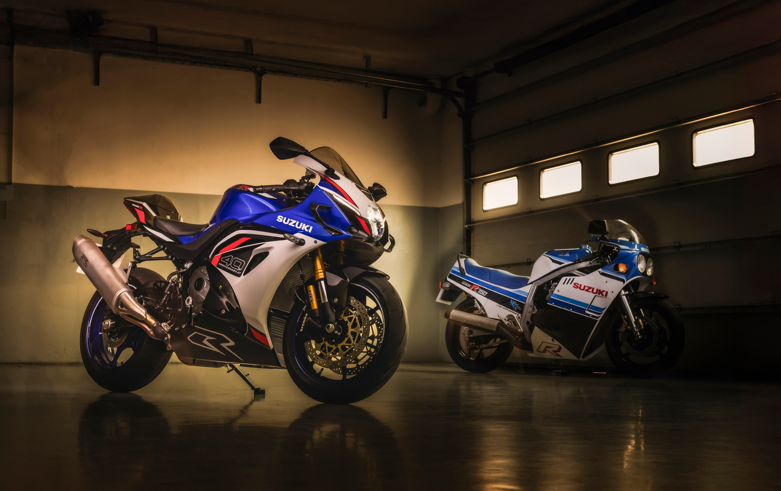 Suzuki GSX-R1000R blue, in a pit box with a classic GSX-R750 in the background.