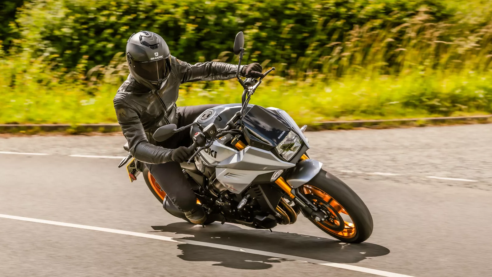 Suzuki Katana silver coming into a corner front three quarters with bushes behind
