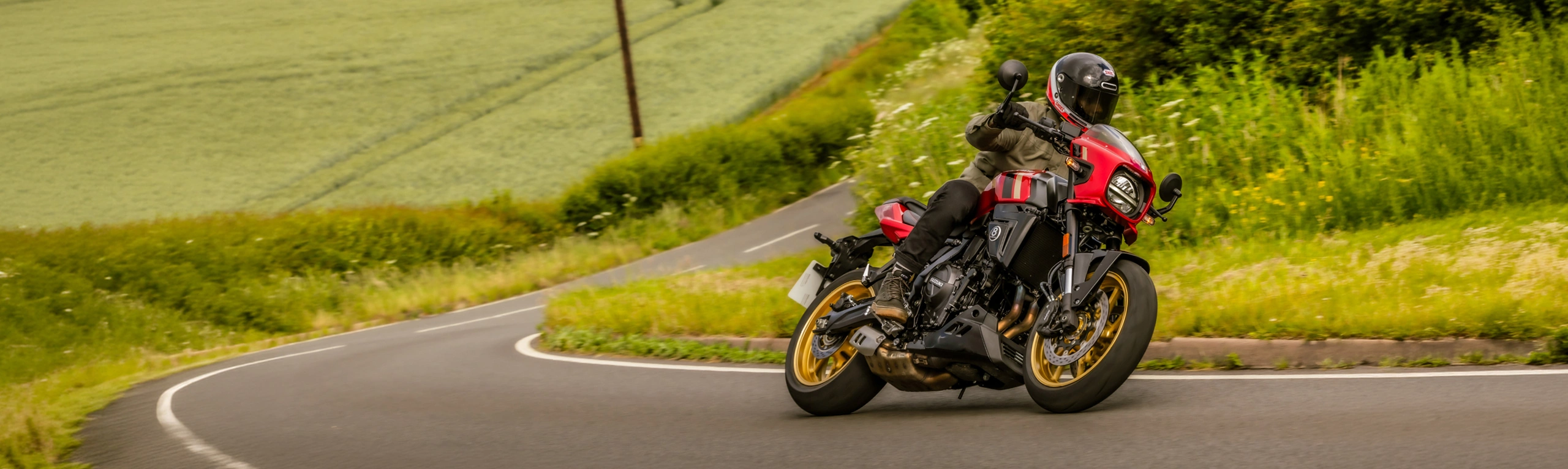 Suzuki GSX-8TT red pushing through a corner with bushes, trees and fields behind
