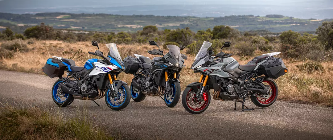 Suzuki GSX-S1000GX+ three colour line-up with bikes static and a wood in the background.