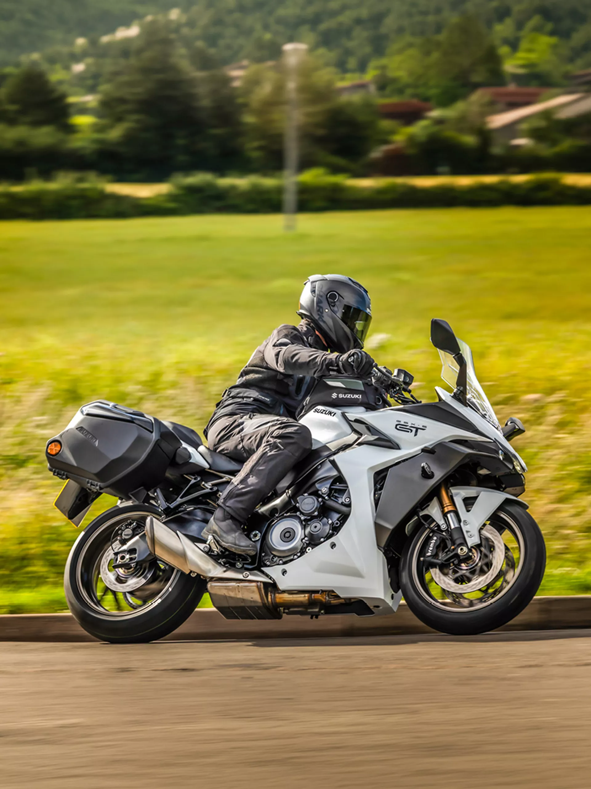 Suzuki GSX-S1000GT+ leaning into a corner with a green field behind.