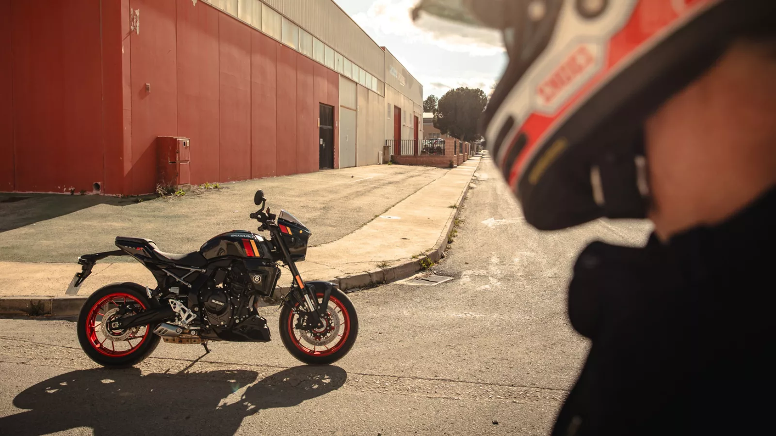 Suzuki GSX-8TT static with the rider looking back at their bike with a red wall behind