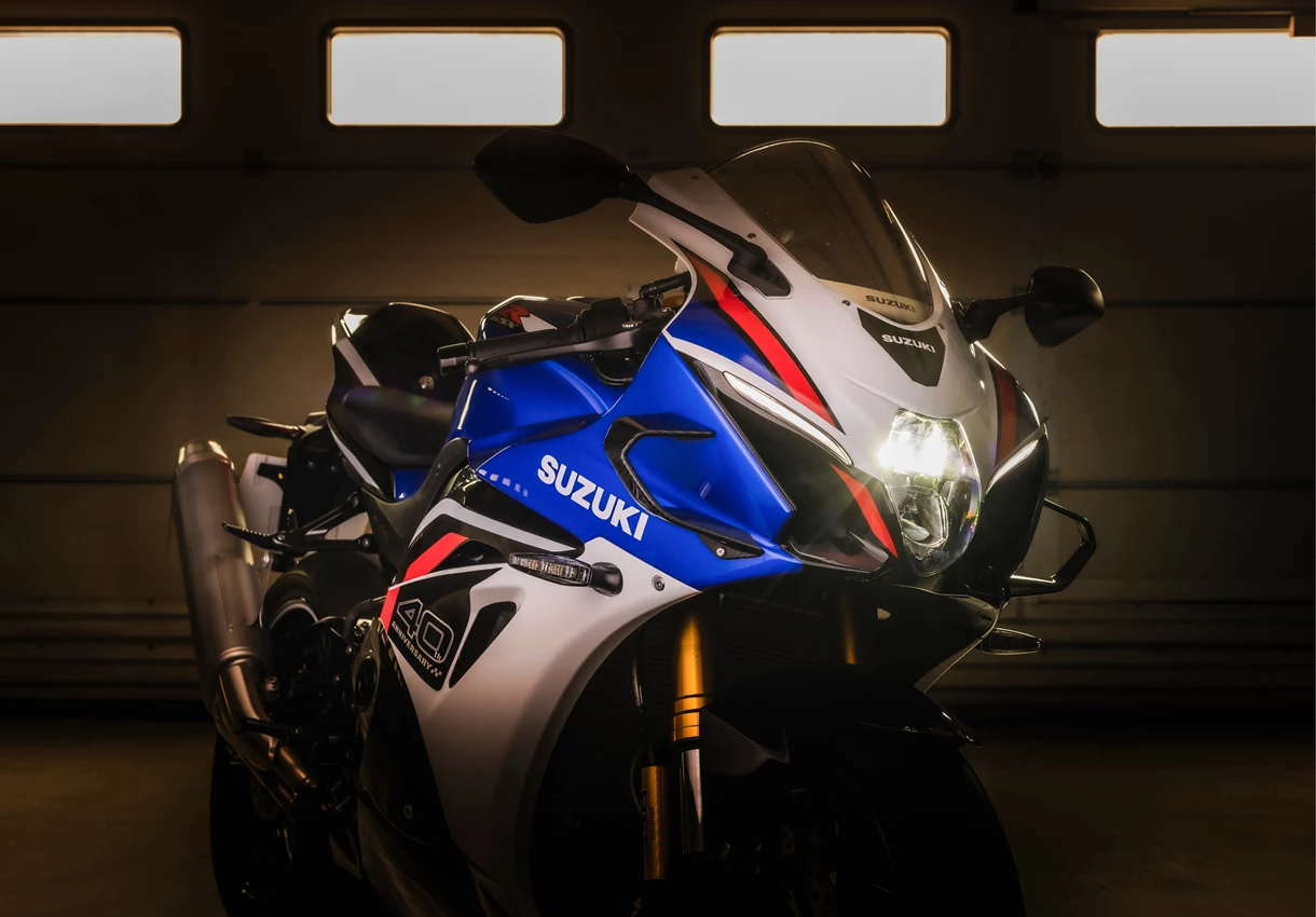 Suzuki GSX-R1000R front three quarter in a dark pit garage with headlight on
