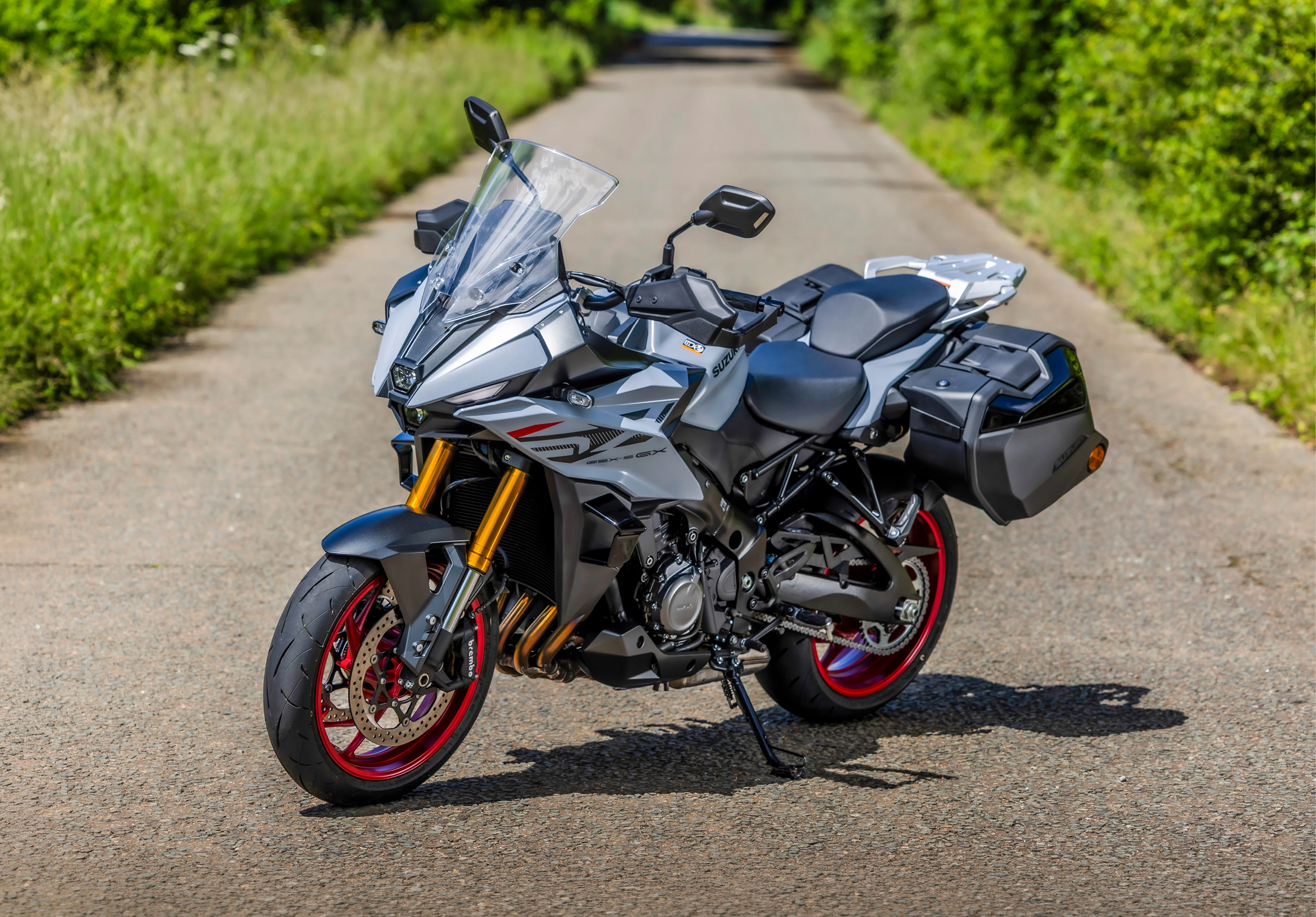 Suzuki GSX-S1000GX+ staic left hand side front three quarters with tree lines road behind.