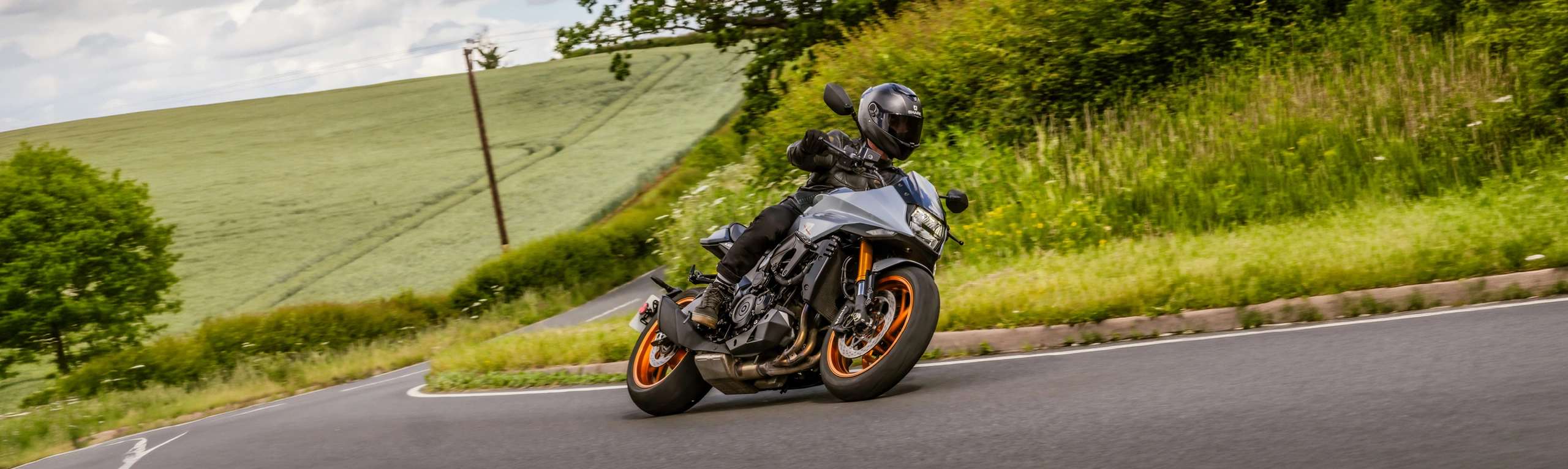 Suzuki Katana silver leaning into a corner with rolling countryside and trees behind