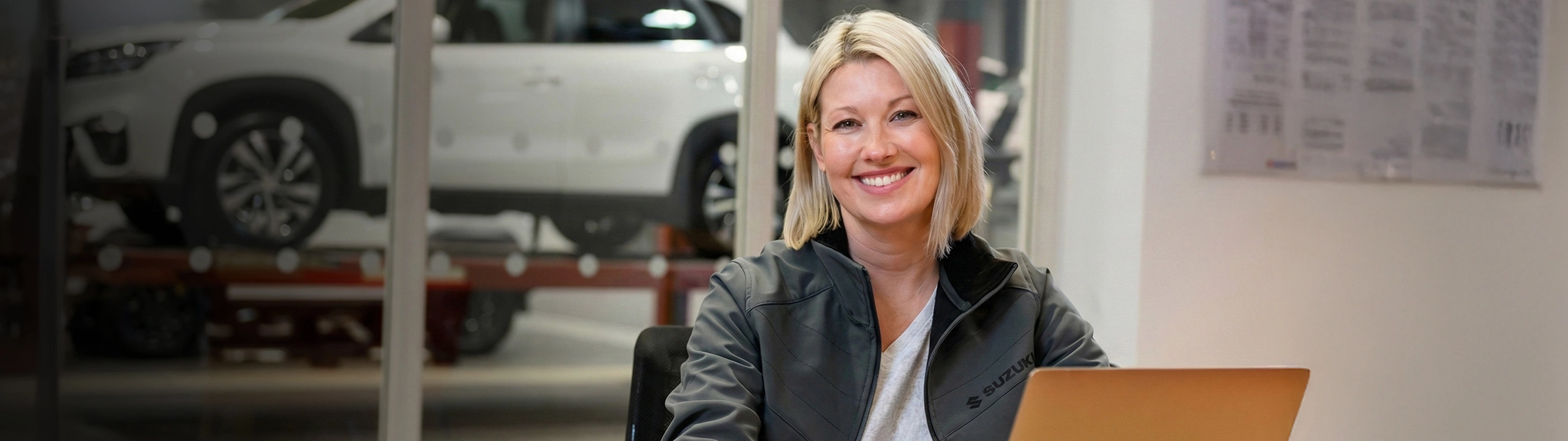 Suzuki employee sitting at a desk with a laptop inside a dealership showroom