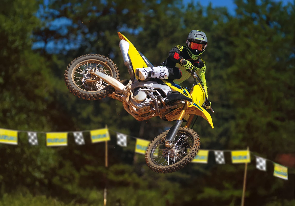Suzuki RM-Z250 whip over a jump with trees in the background