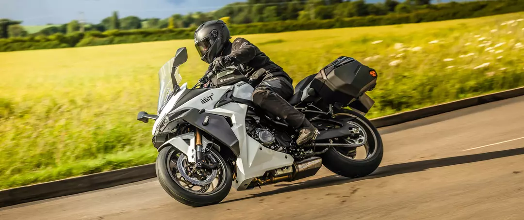 Suzuki GSX-S1000GT+ leaning into a corner on a country road.