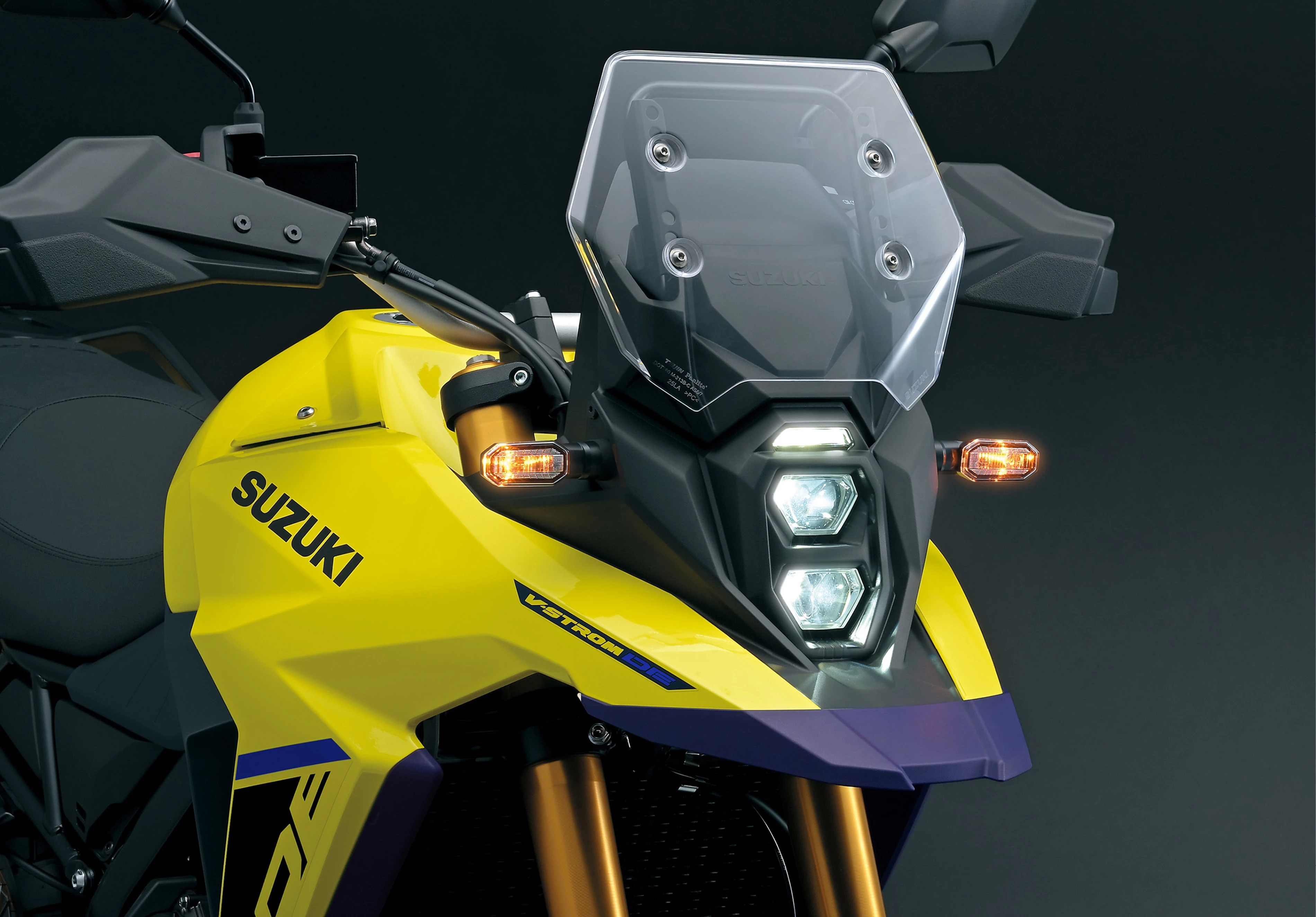 Close-up of the Suzuki V-Strom 800DE’s front cowl and headlights, showing off its distinctive triple-LED layout and angular fairing design.