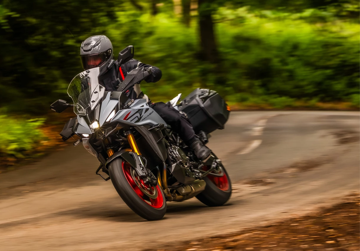 Suzuki GSX-S1000GX+ leaning into a corner on a forest lined road. 