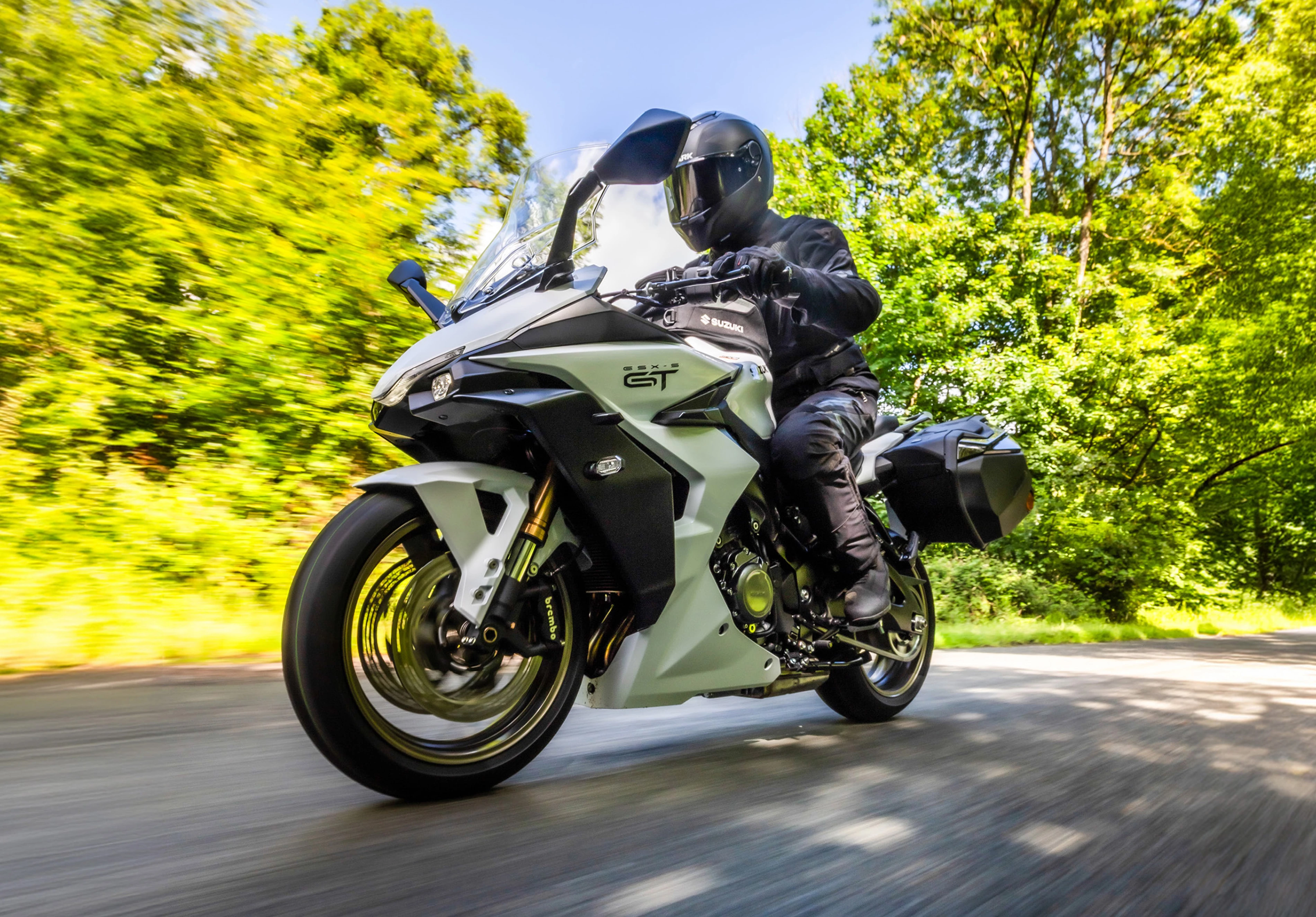 Suzuki GSX-S1000GT+ moving along a tree lined road, low down image from the front left