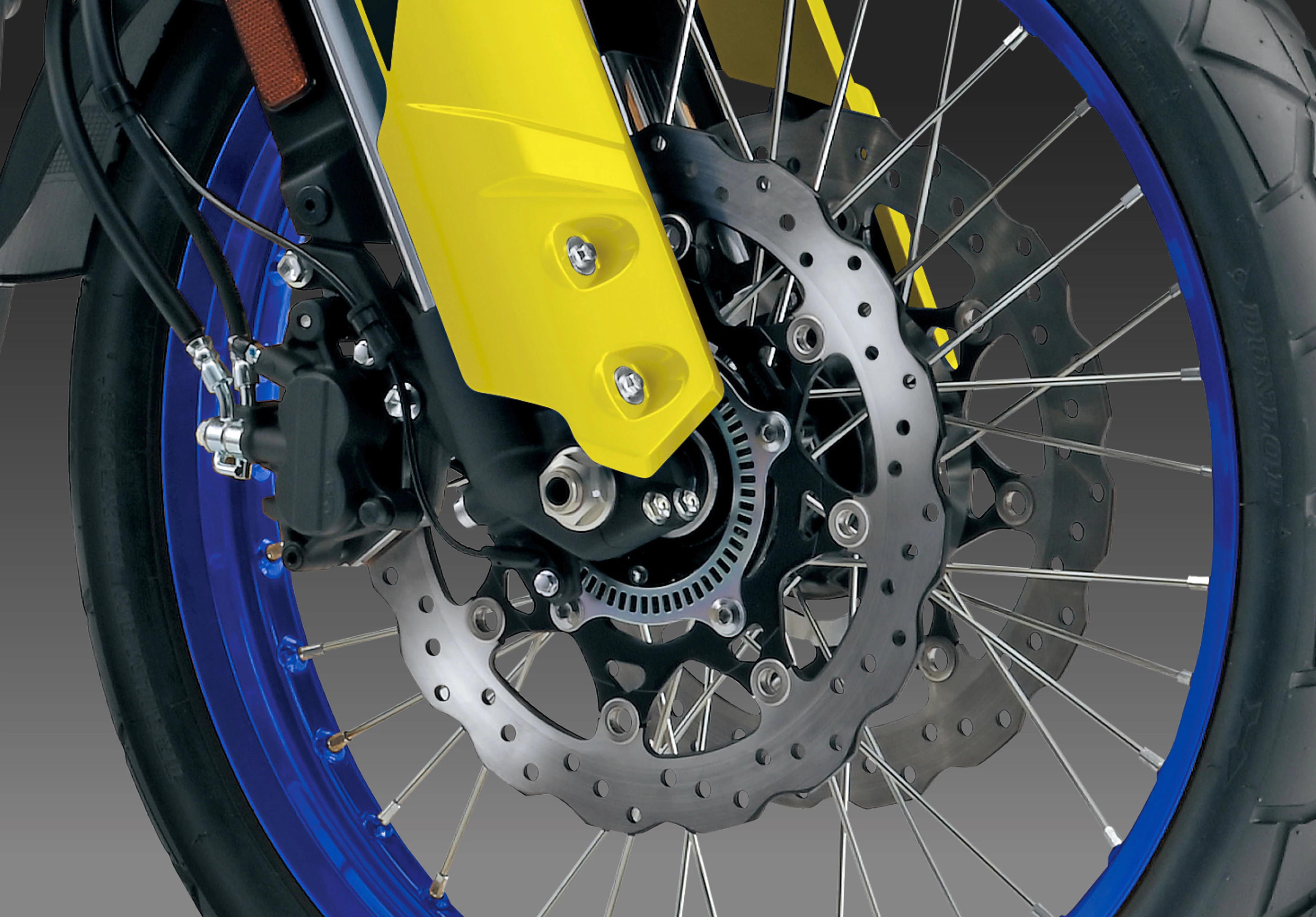 A close-up of the Suzuki V-Strom 800DE front wheel, showcasing its suspension system, brake calipers, and spoke design.