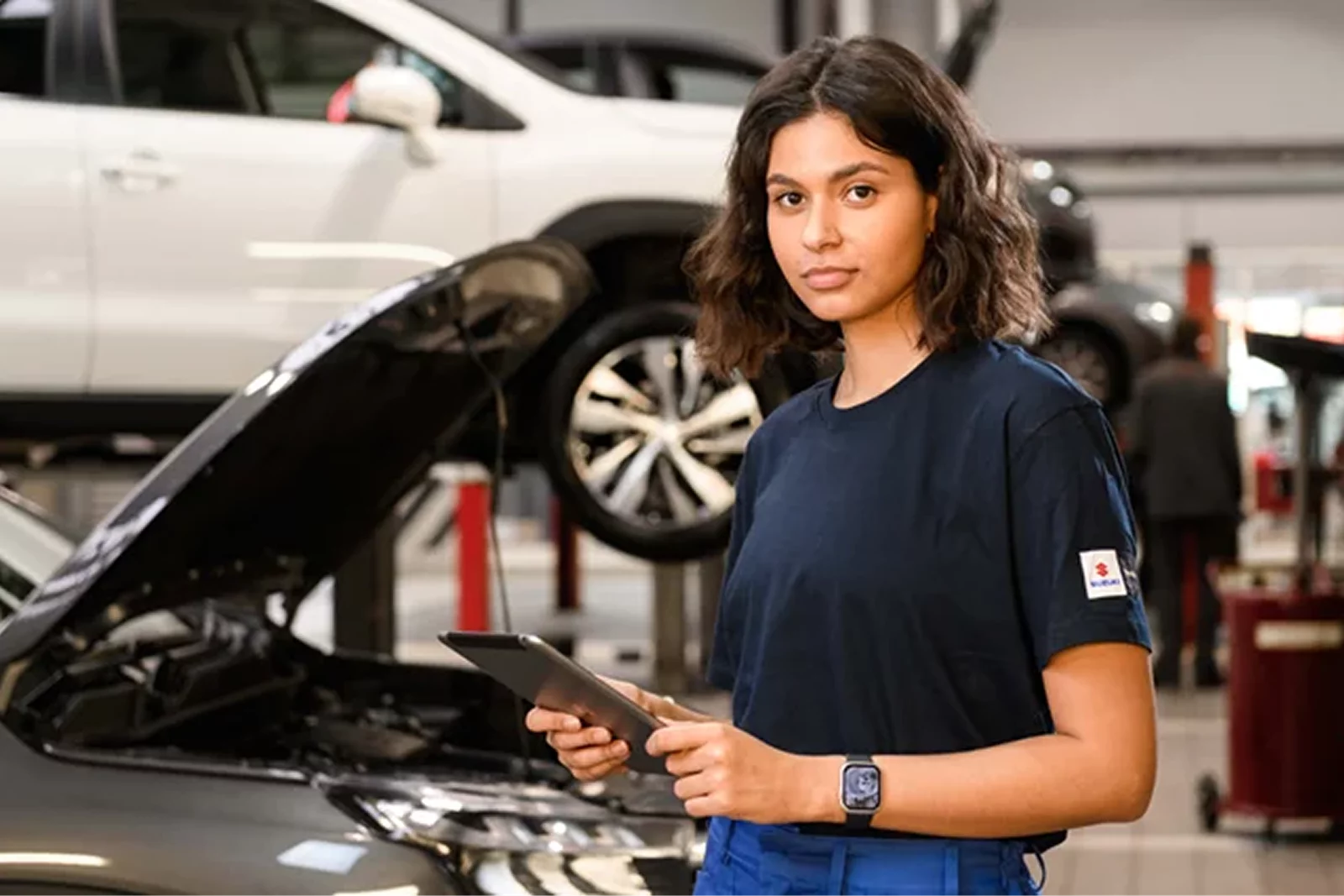 Suzuki service technician holding a tablet beside a car in a workshop