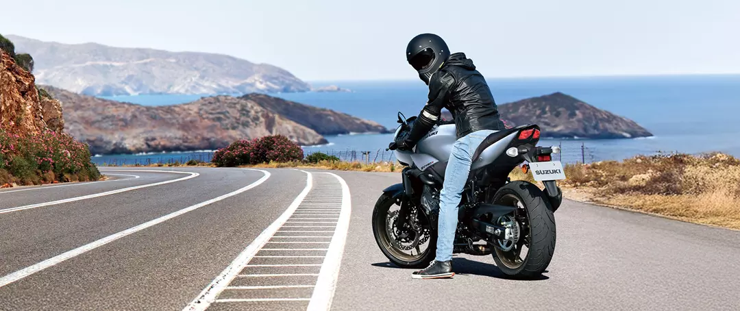 Suzuki SV650X stopped on a corner with the rider looking back and a coastal background