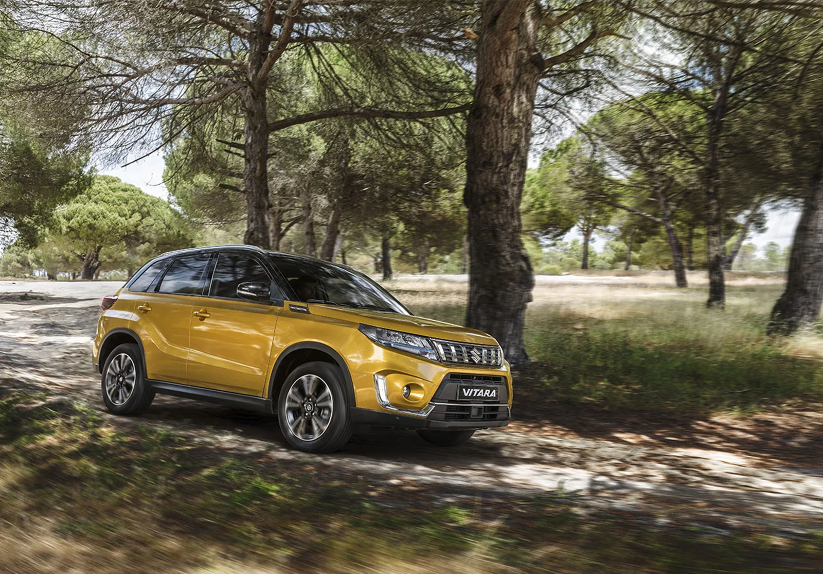 Solar yellow Suzuki Vitara cruising down a scenic countryside road