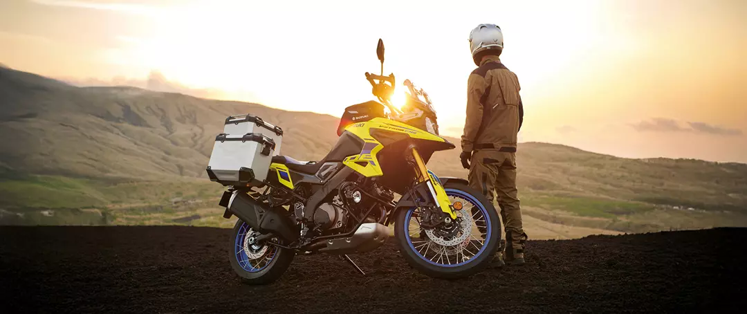 Suzuki V-Strom 1050DE sunset side on image with rider standing in front of the bike