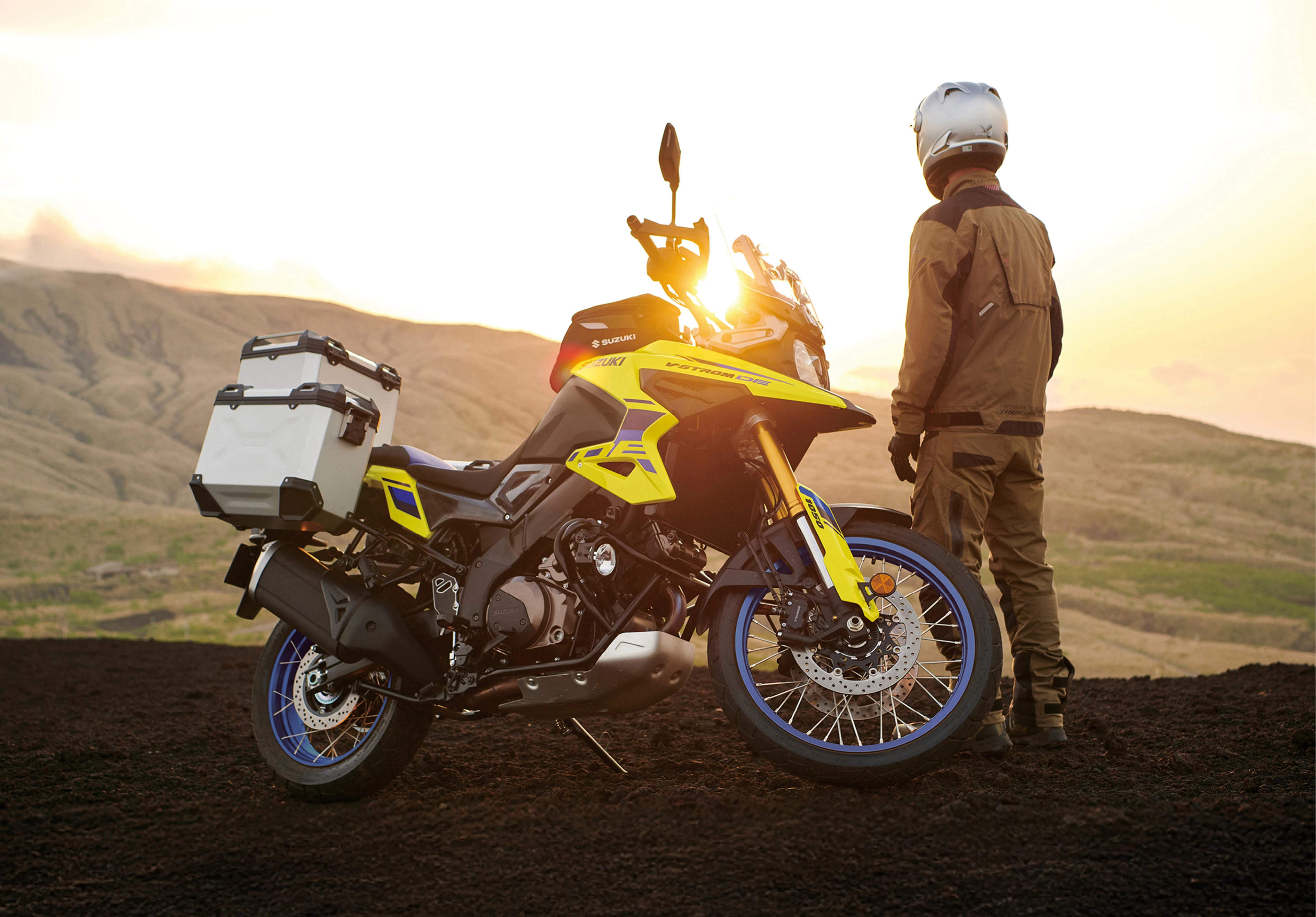 Suzuki V-Strom 1050DE sunset side on image with rider standing in front of the bike