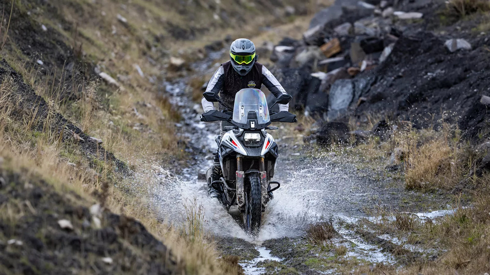 Suzuki V-Strom 1050DE white moving through a water splash on a mountain trail