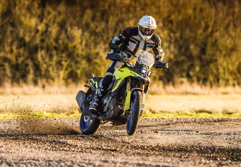 A front-facing shot of the Suzuki V-Strom 800DE tackling a gravel path, with the rider standing for better stability and control.