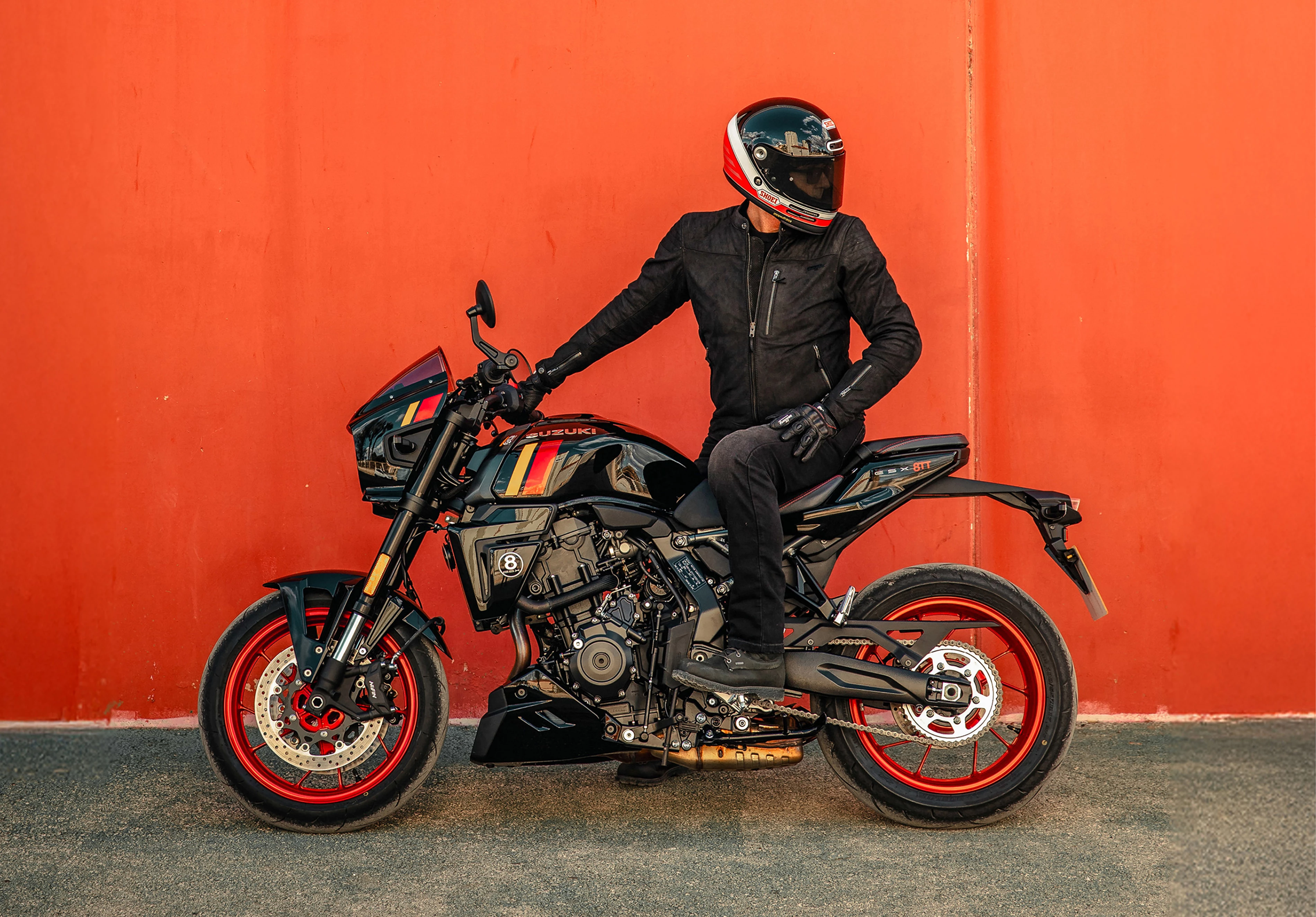 Suzuki GSX-8TT right hand side static with rider looking away, red door background