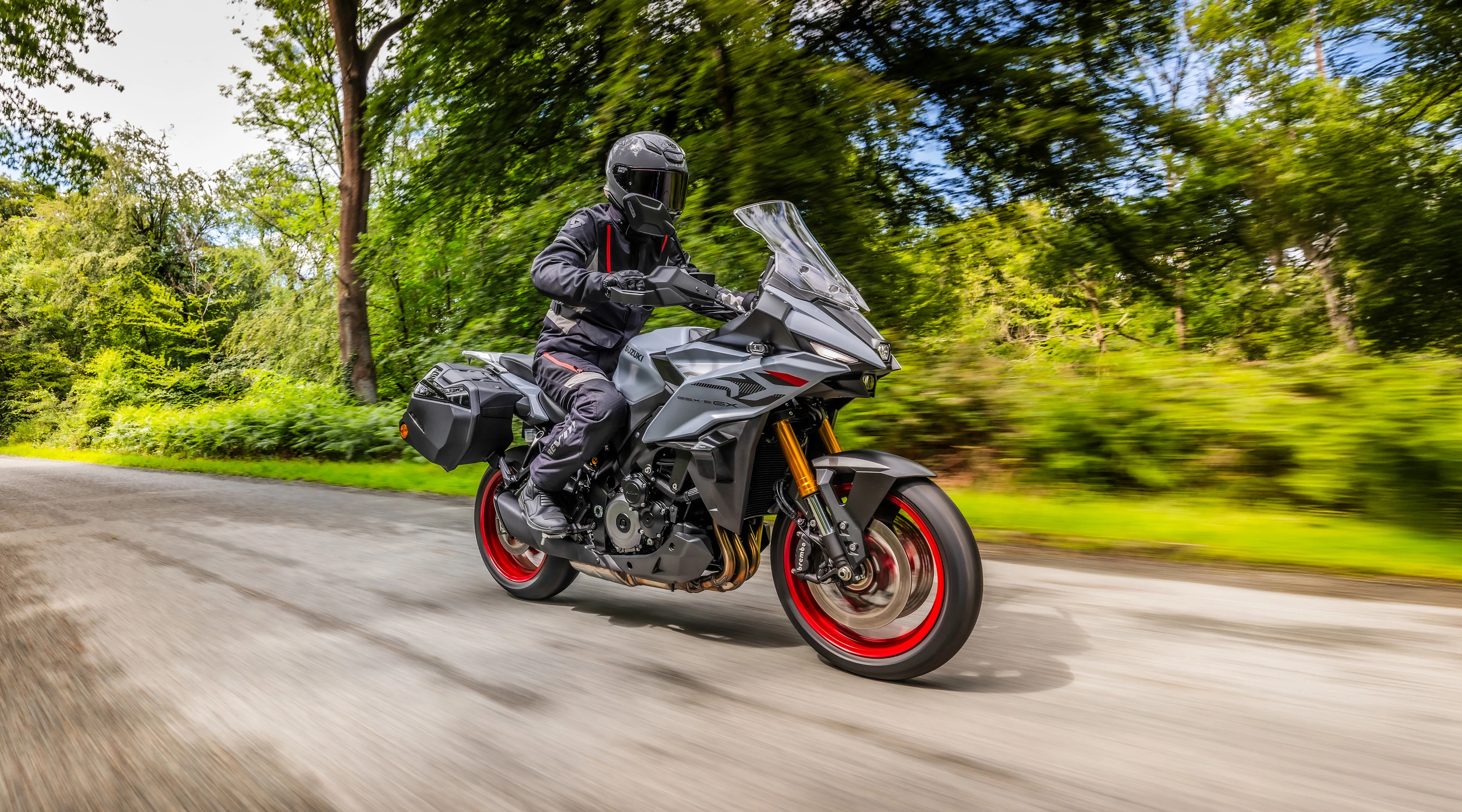 Suzuki GSX-S1000GX+ riding along a country road lined by trees.