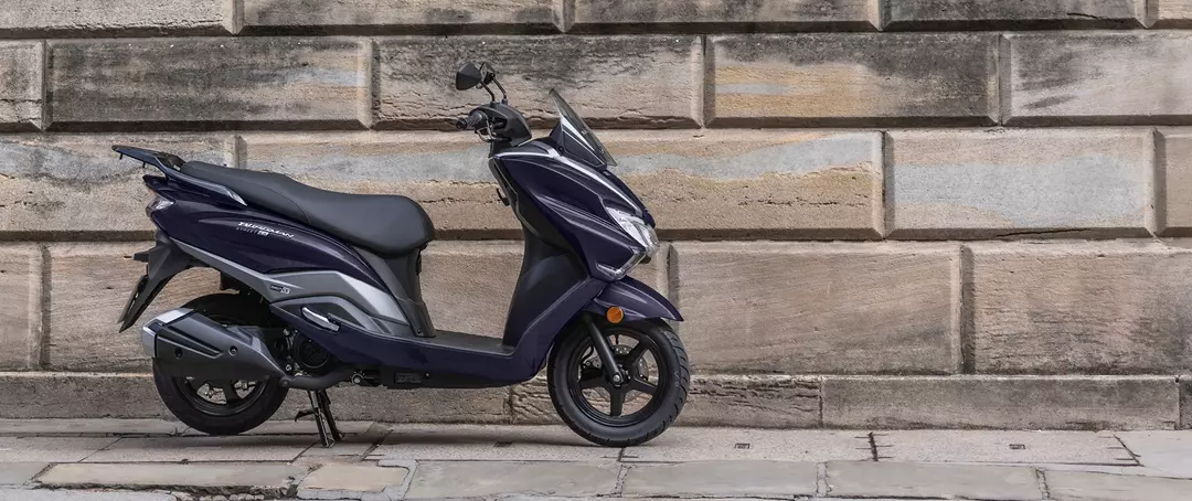 Suzuki Burgman Street 125EX side profile parked against a textured stone wall, highlighting its stylish and compact frame.
