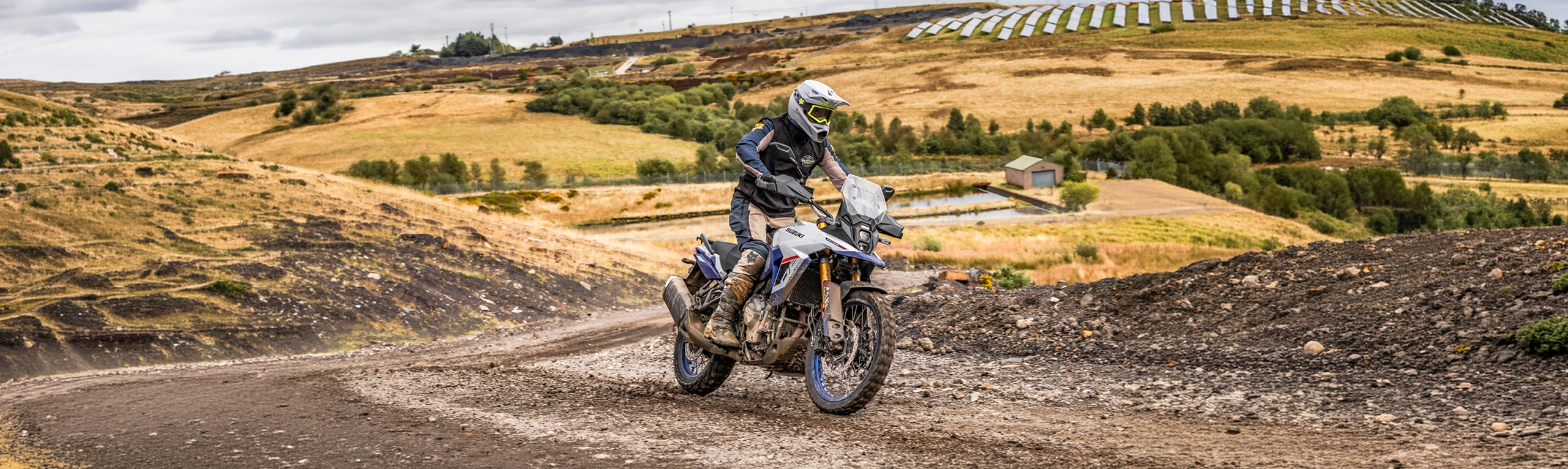 Suzuki V-Strom 800DE pushing on along a dirt trail with hills behind