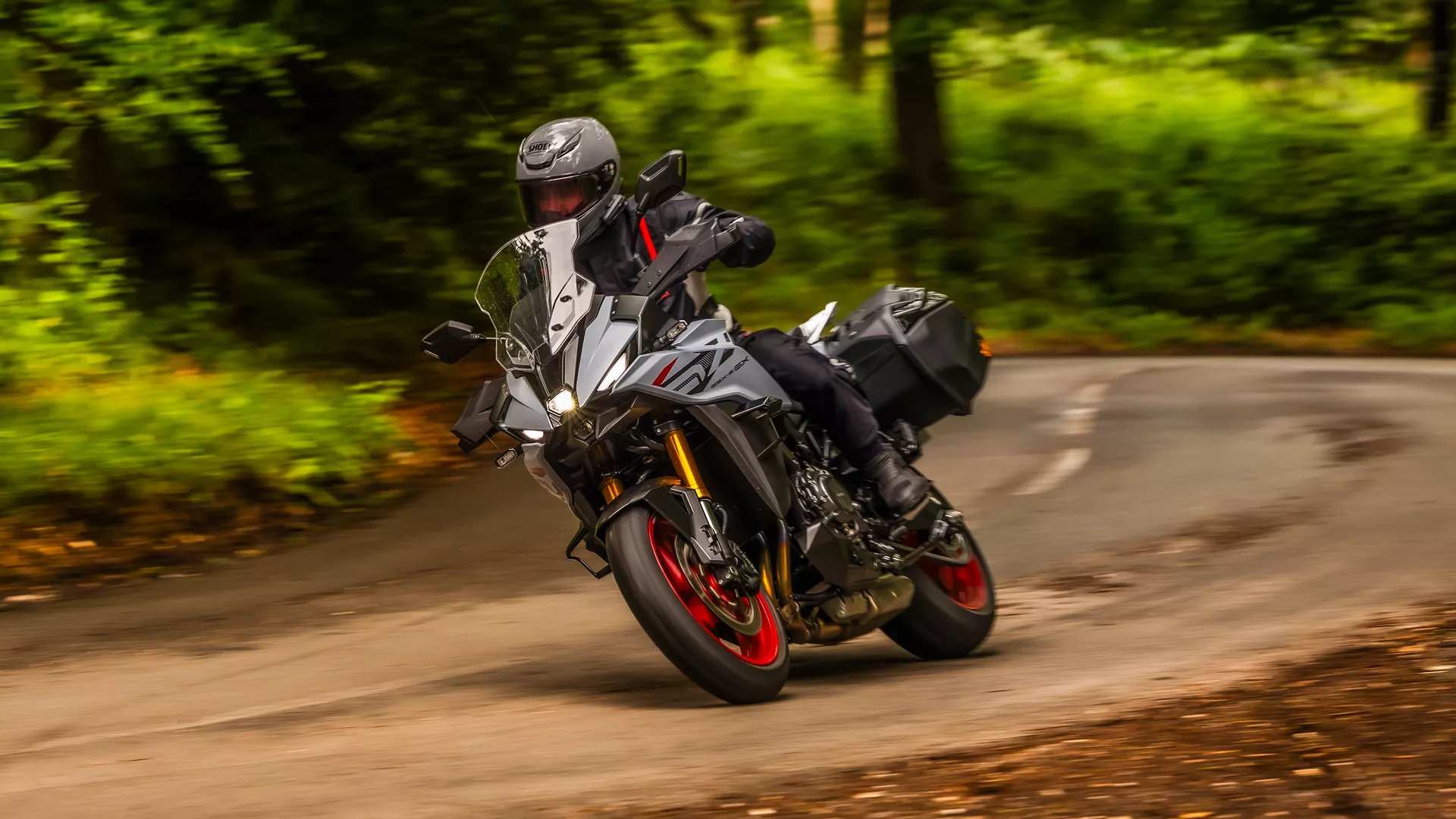 Front three quarter image of a Suzuki GSX-S1000GX+ riding through a right hand bend through the trees.