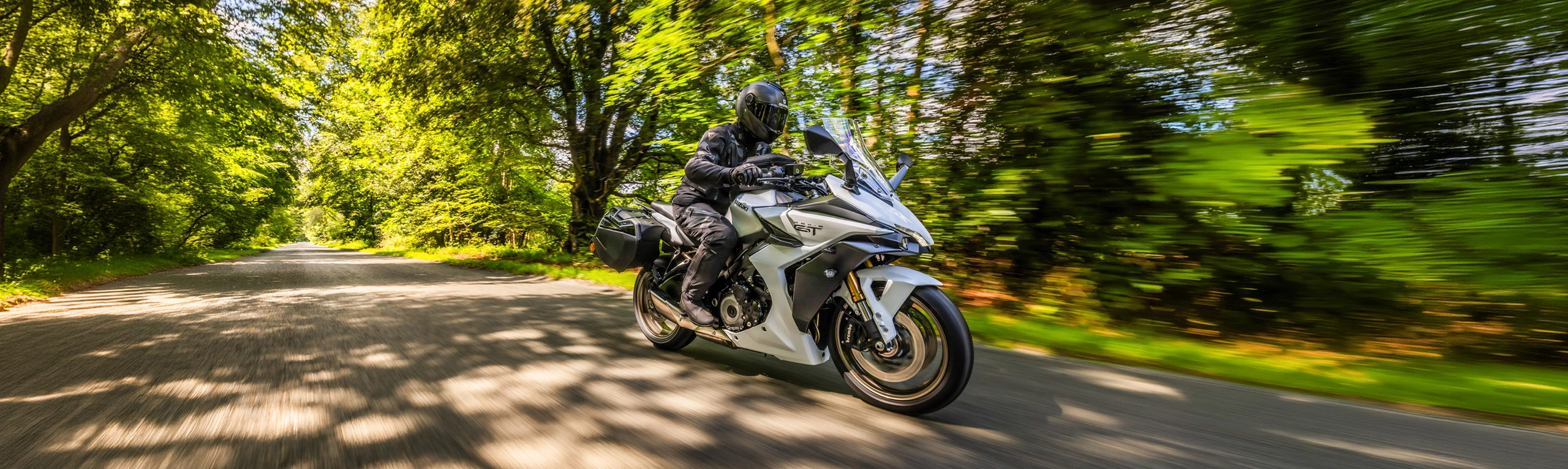 Suzuki GSX-S1000GT+ white moving along a tree lined road