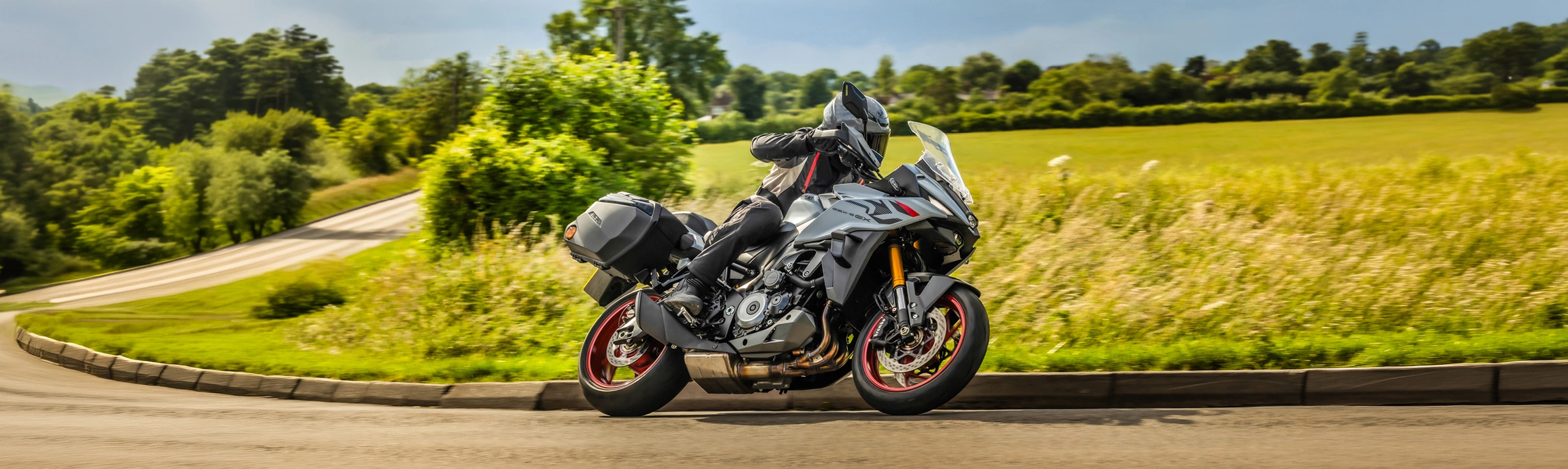 Suzuki GSX-S1000GX+ rounding a corner with golden field and trees behind