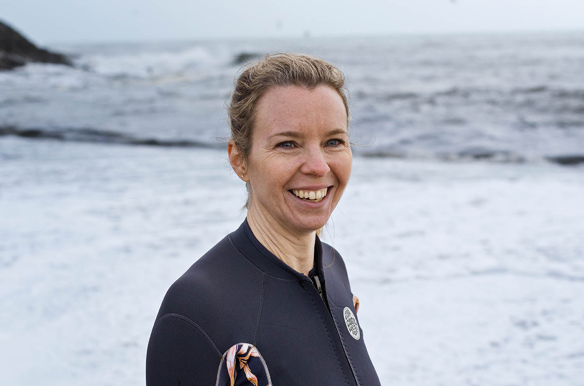 Woman in wetsuit smiling by the sea