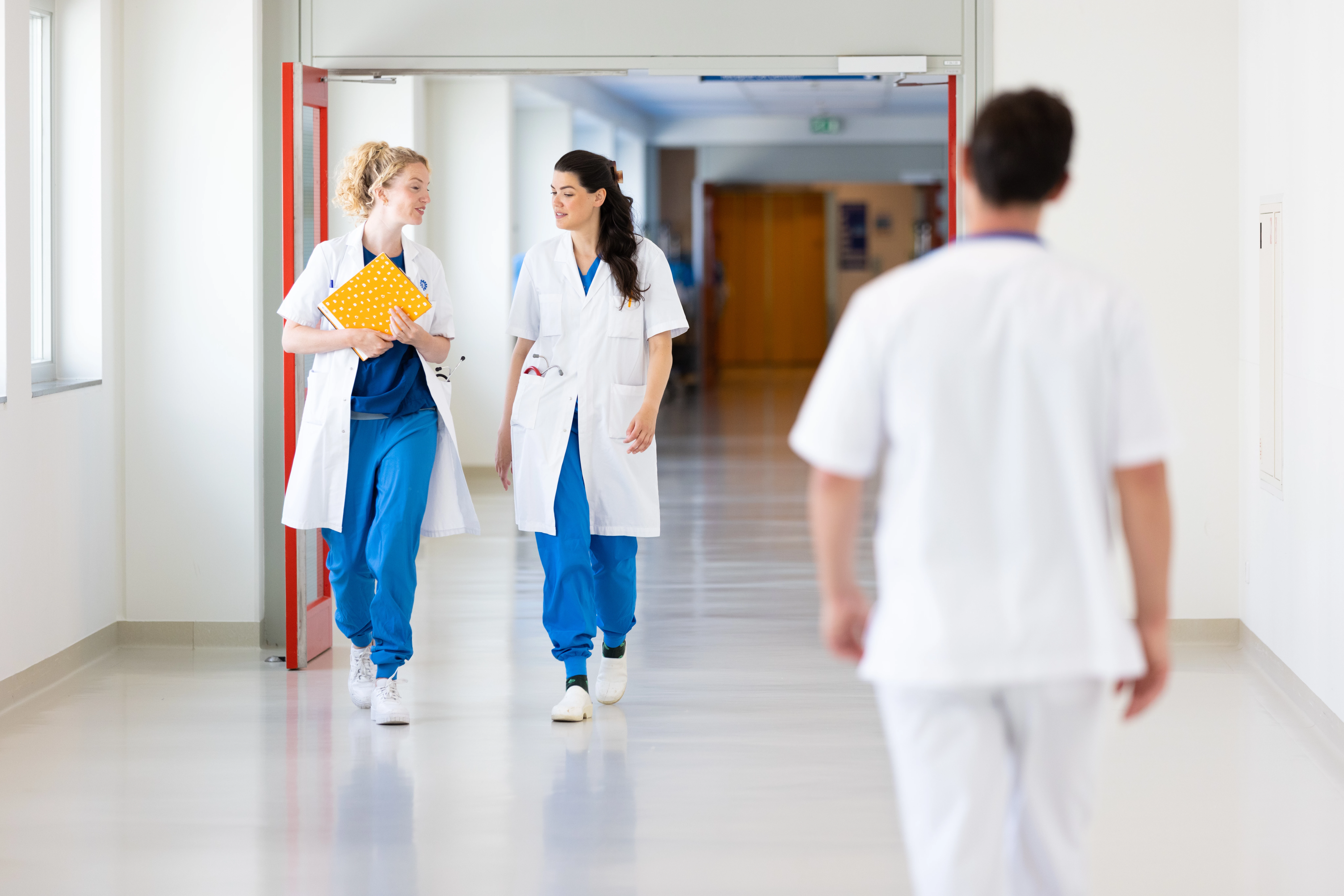 2 jonge zorgprofessionals in de gang van een ziekenhuis