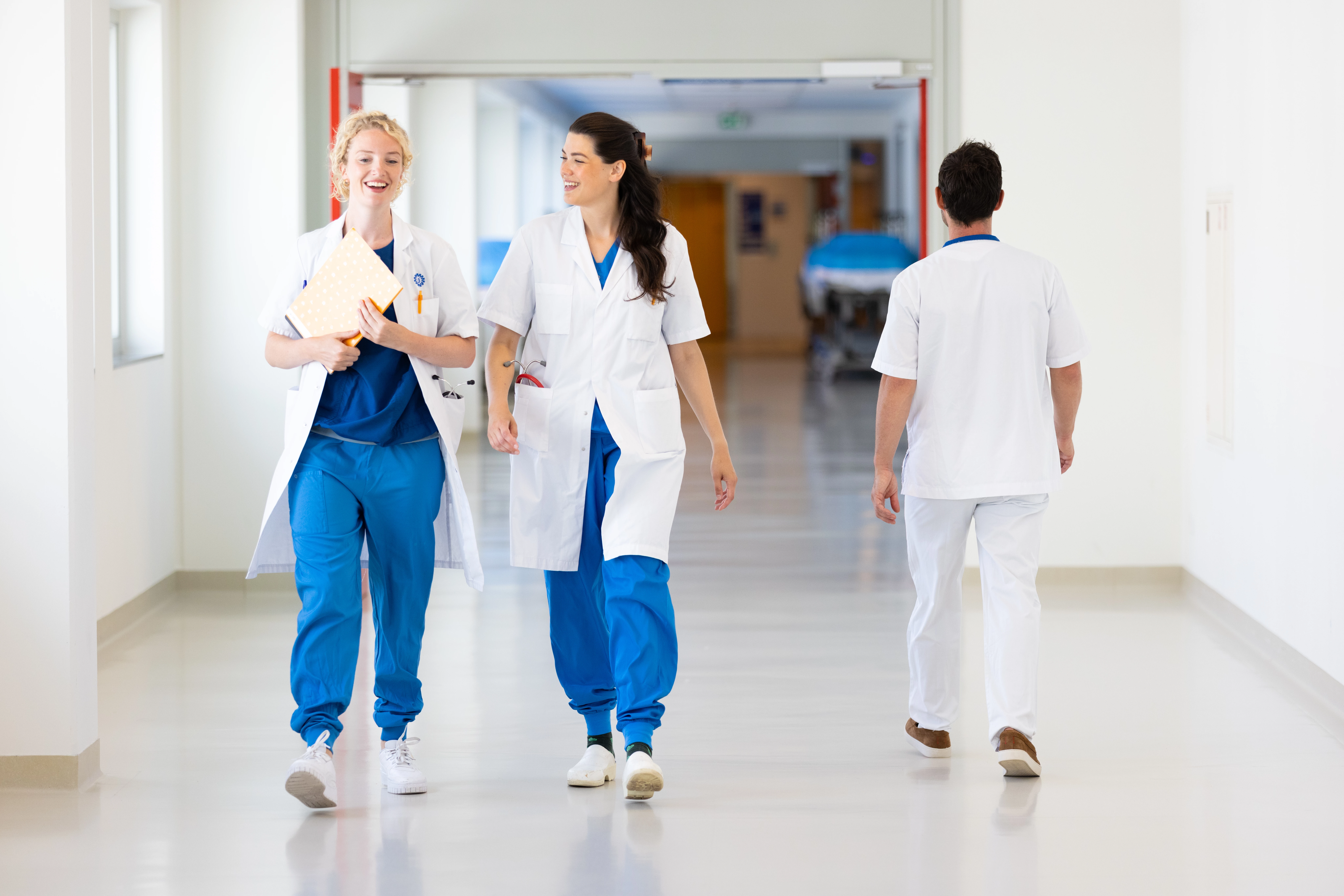 Twee vrouwelijke geneeskunde studenten lopen in witte jas door de gangen van het ziekenhuis