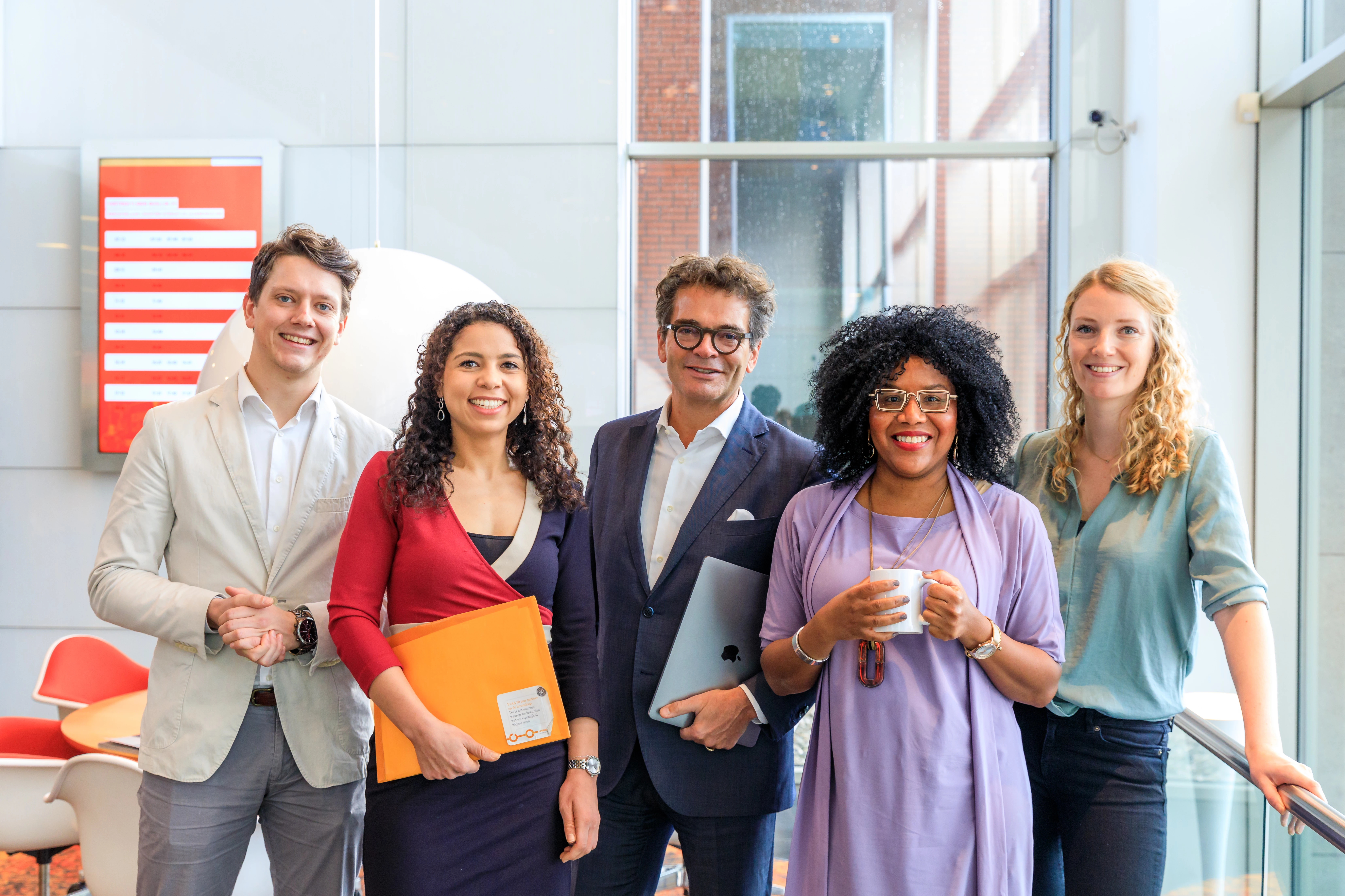 Twee mannen en drie vrouwen kijken lachend in de camera