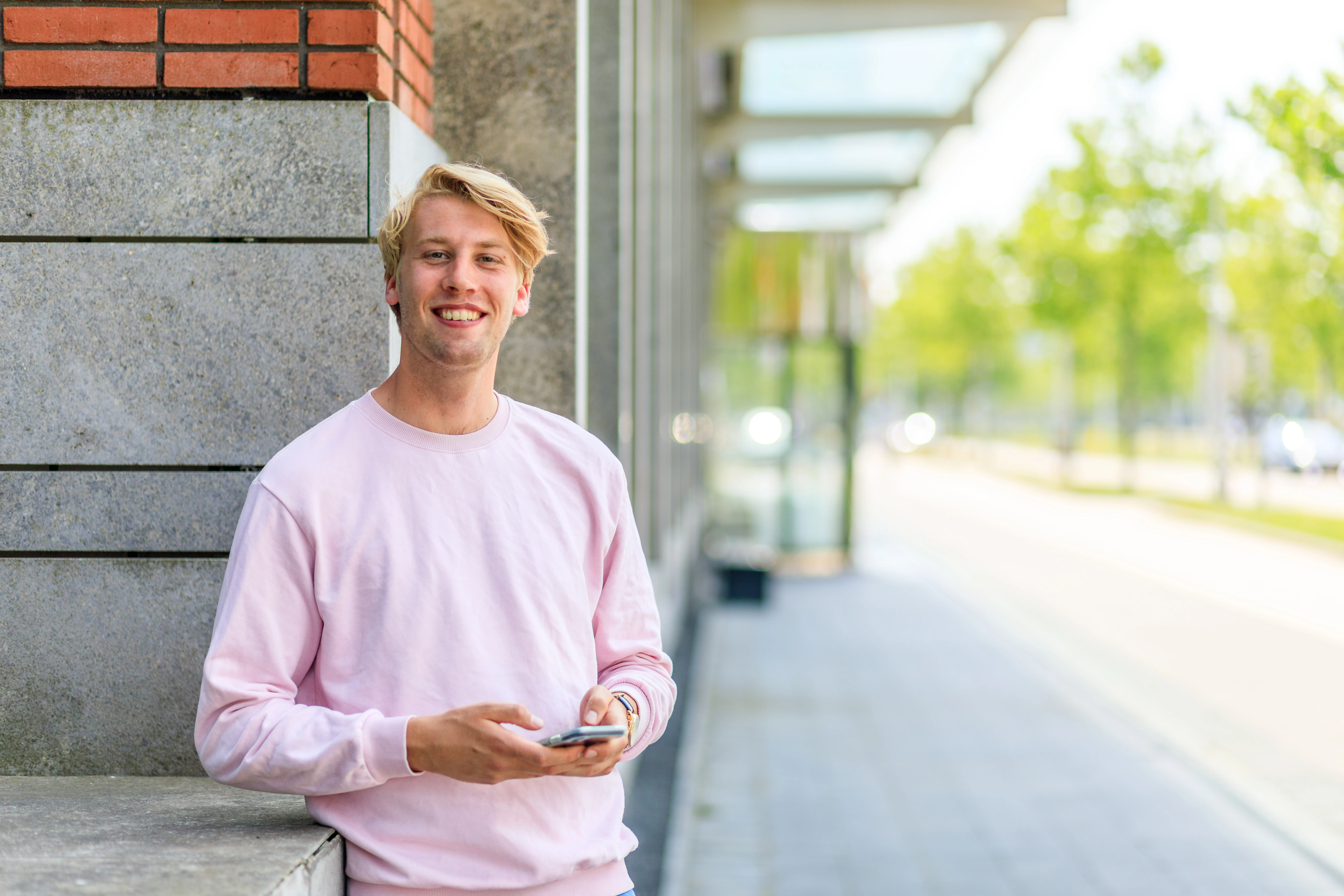 Jongeman met telefoon in zijn hand glimlacht vriendelijk 