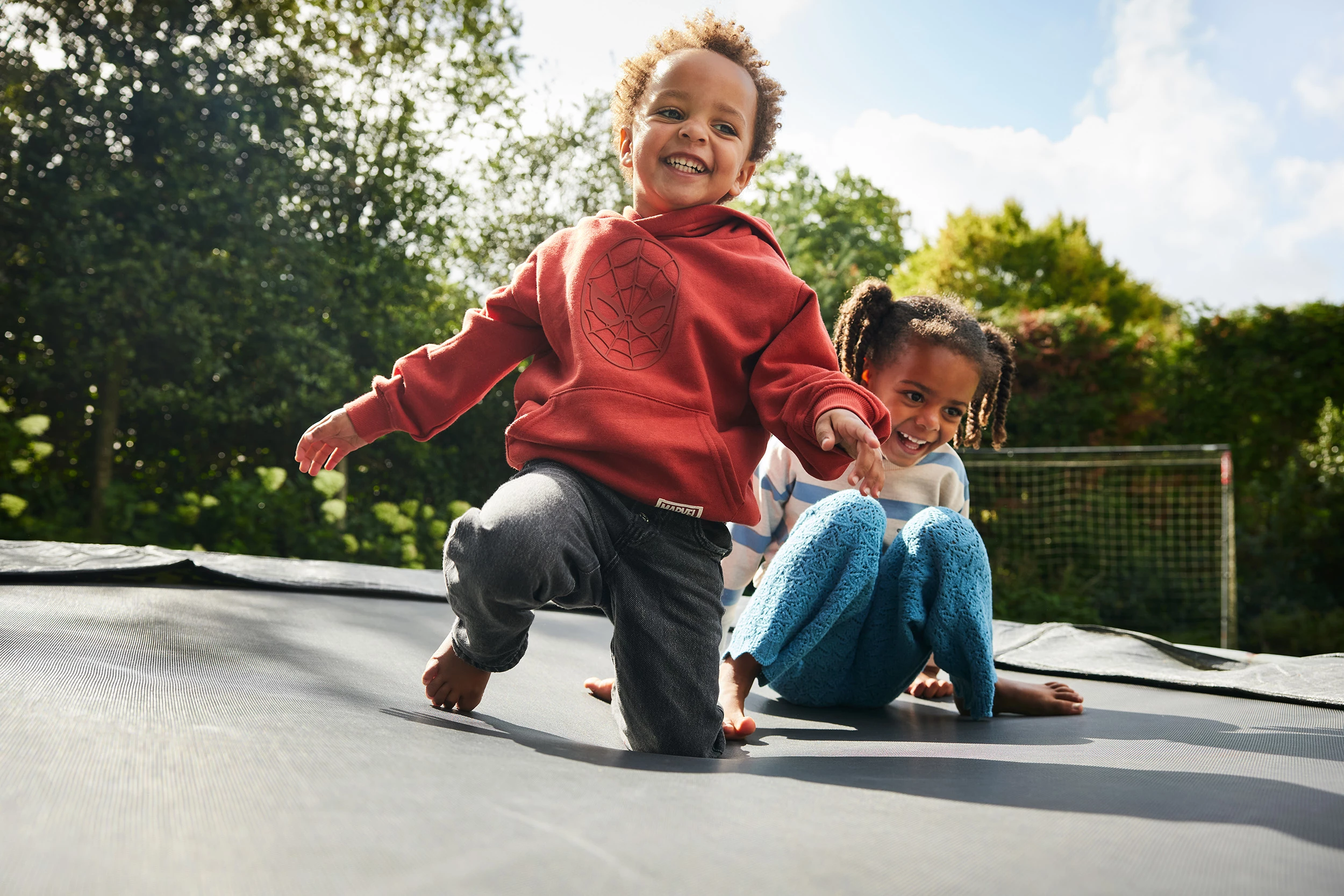 2 lachende kinderen springen samen op de trampoline in de tuin.