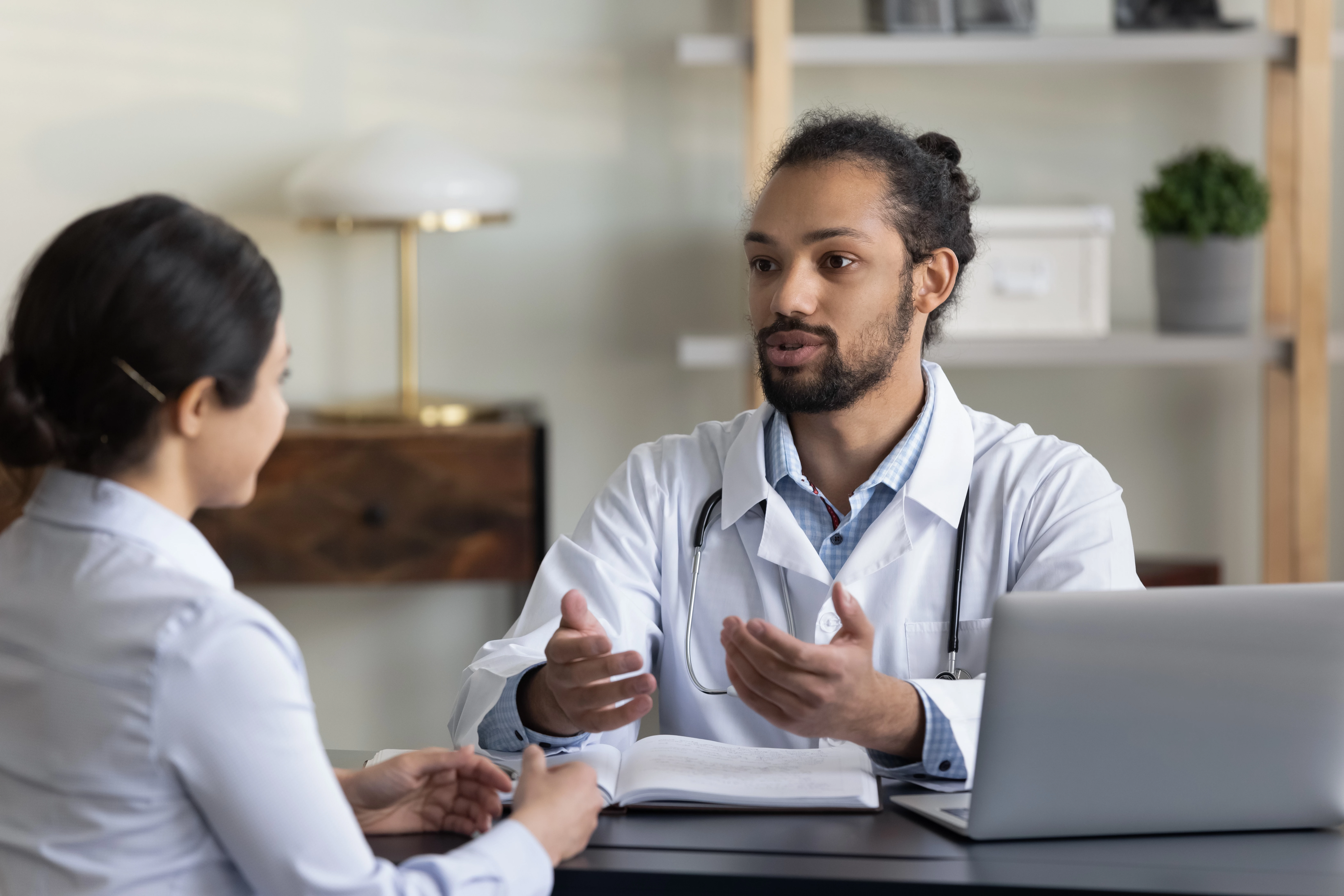 Een vrouw en een man zitten tegenover elkaar aan een zwart bureau en praten met elkaar