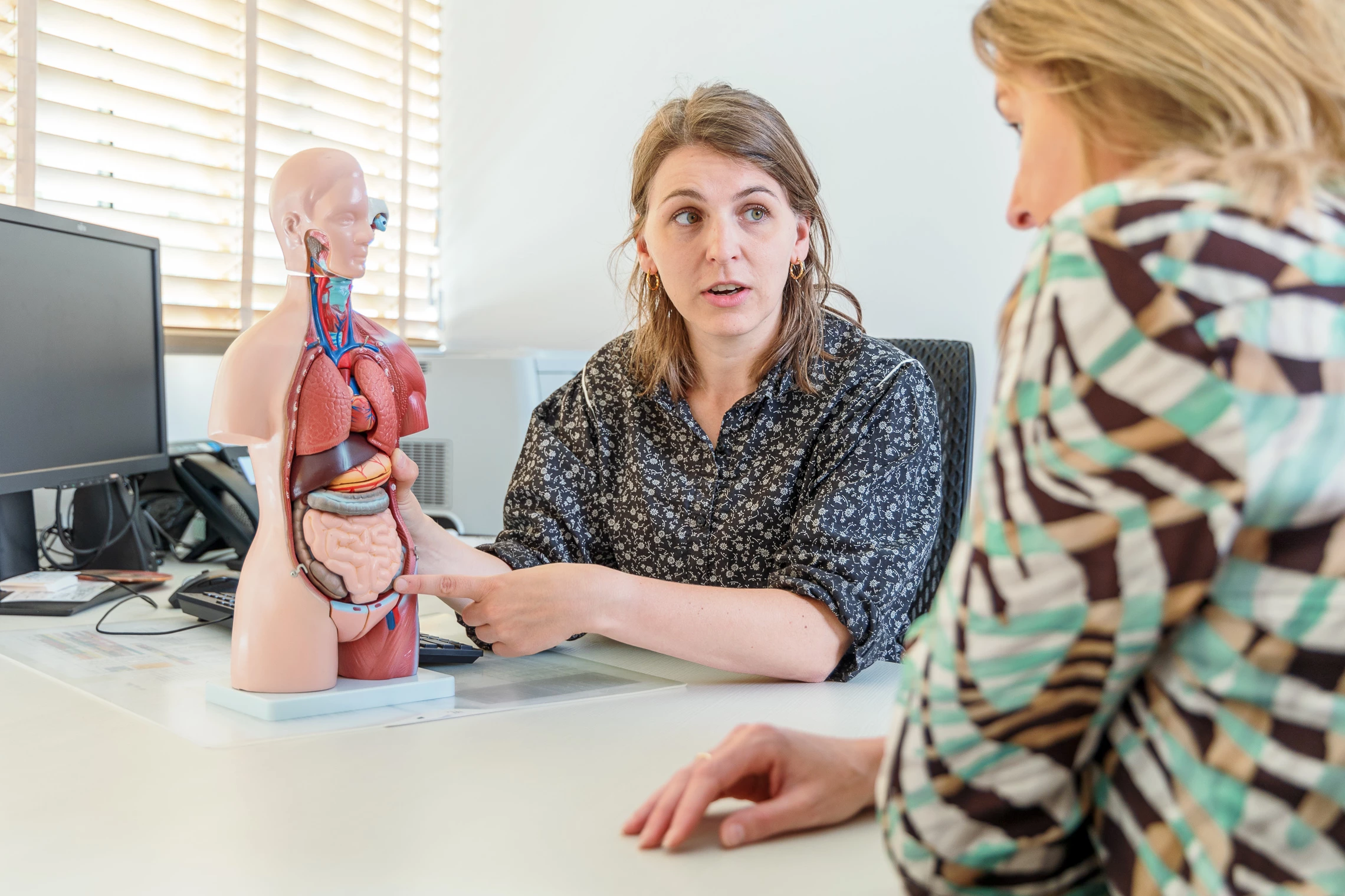 Dokter geeft patiënt via anatomische pop informatie over de behandeling 