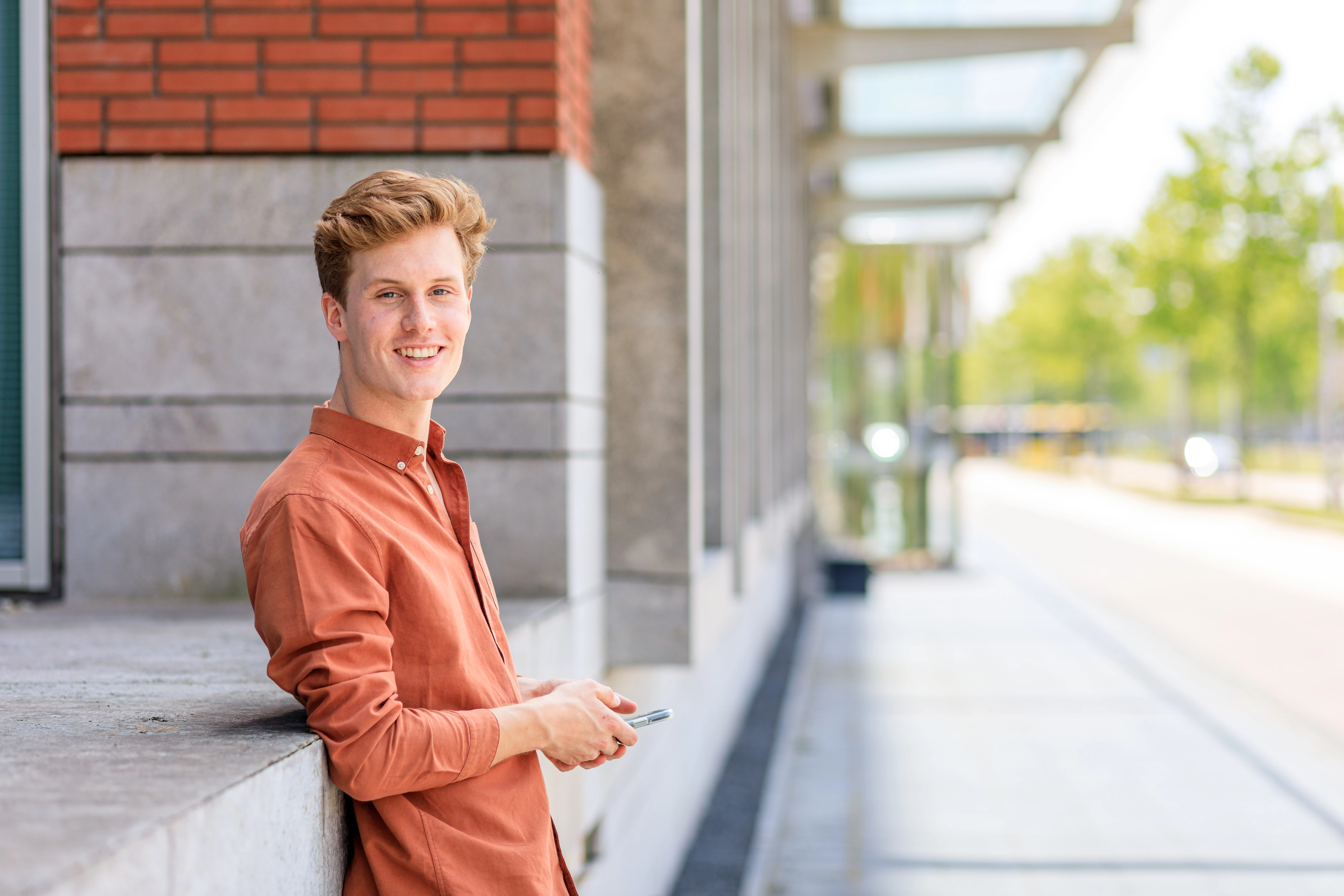 Medisch student leunt tegen muurtje met telefoon in de hand.